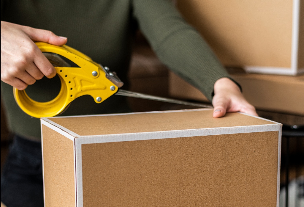 Hands sealing cardboard moving boxes with yellow tape dispenser in Tennessee